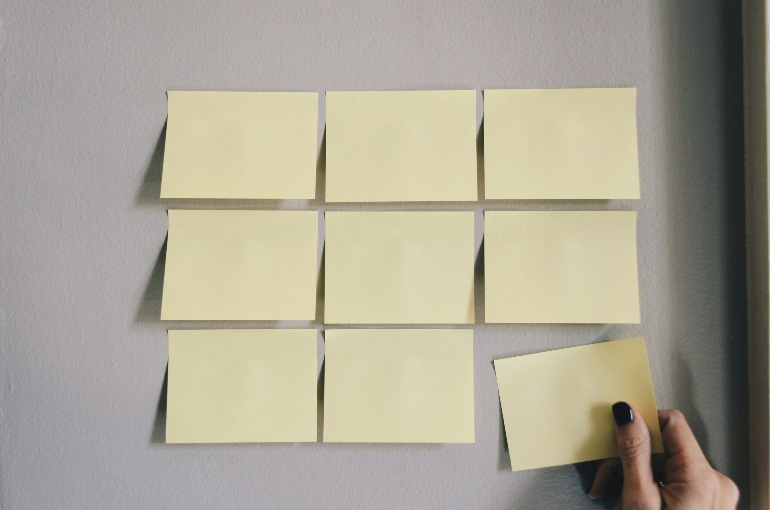 A hand placing a sticky note on a wall, symbolizing the process of organizing and outlining clear rules for a tournament.