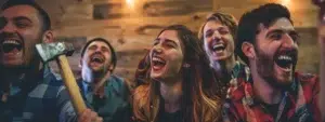 a group of friends laughing and cheering as they successfully throw axes at a target in an axe throwing venue.