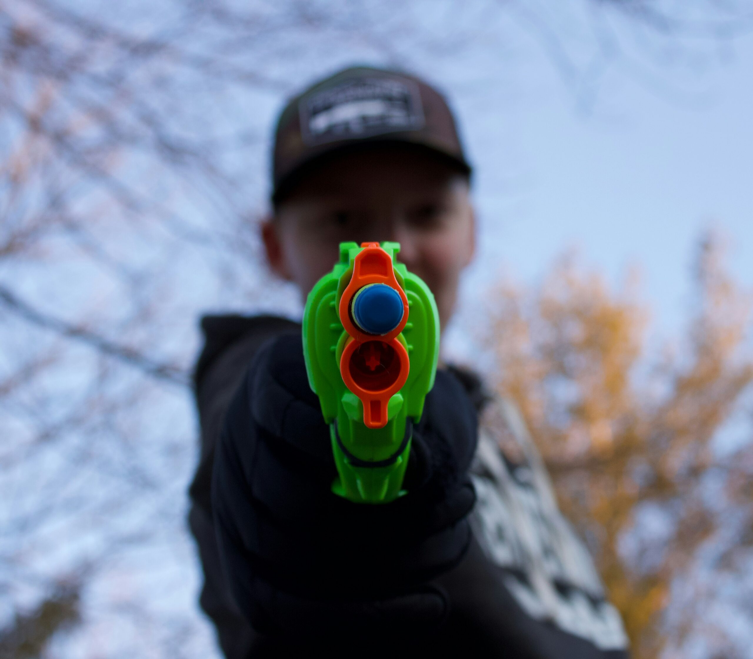 A person aiming a bright green Nerf gun directly at the camera outdoors.