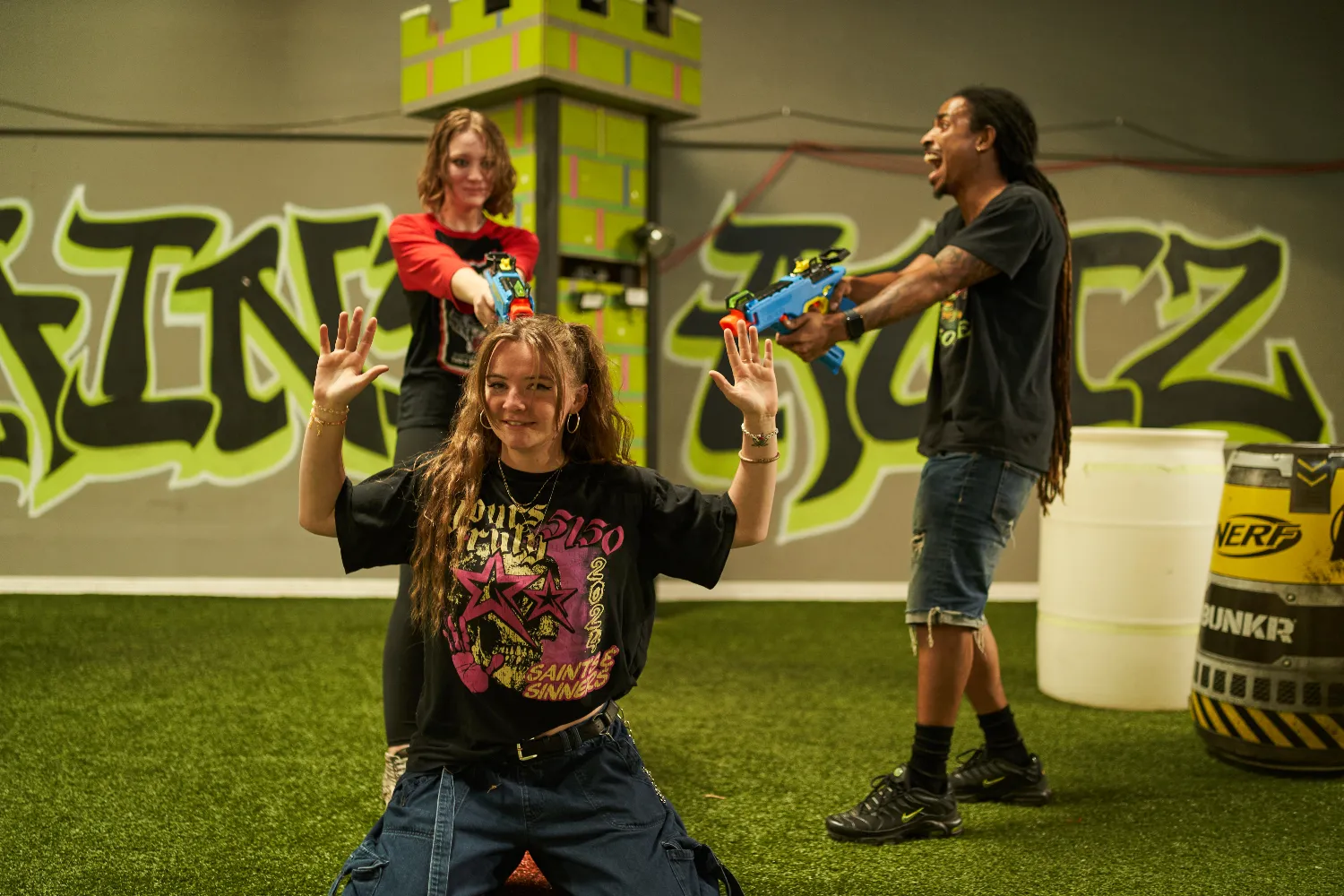 Three people enjoying a Nerf gun battle in a graffiti-decorated indoor arena.