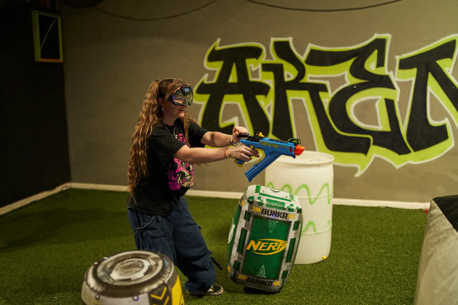 Participant actively engaging in a Nerf war, maneuvering around obstacles and using a Nerf Rival blaster in a themed arena.