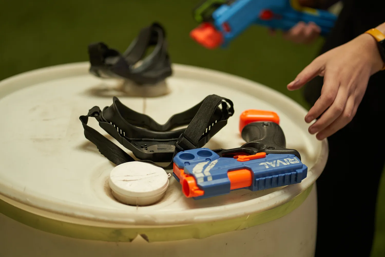 Nerf blaster and safety goggles on a table, with a player reaching for the gun, ready for a game.