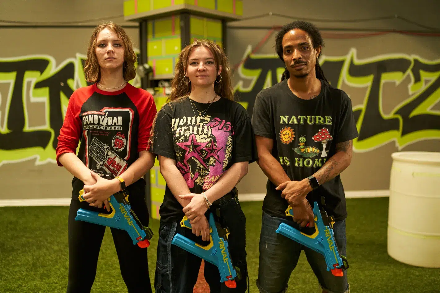 Three players posing with Nerf blasters in front of a vibrant graffiti wall at an indoor Nerf war arena.