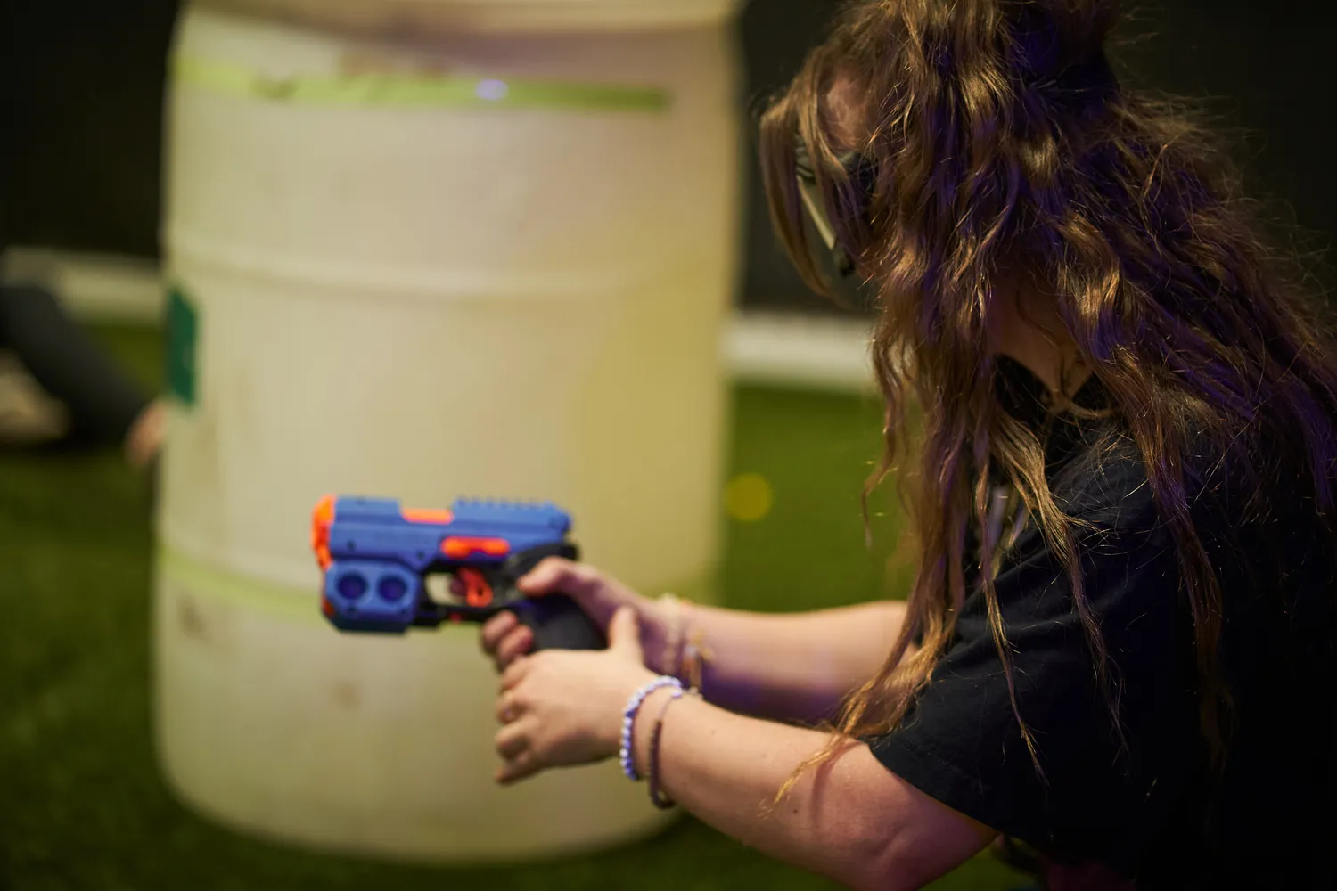 Player crouching and aiming a Nerf gun in an indoor arena, demonstrating the accessibility and fun of affordable Nerf play.