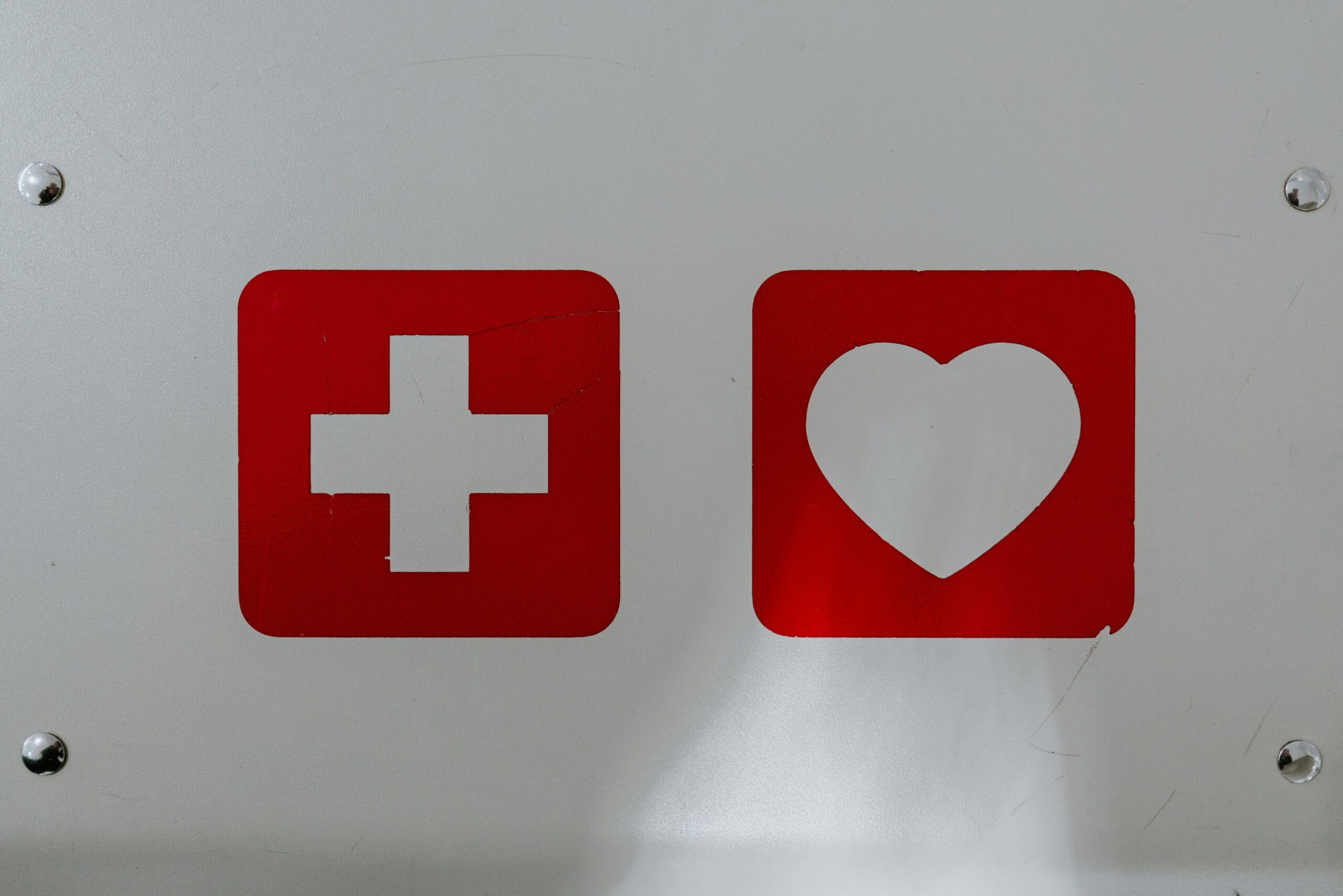 A close-up of emergency signs indicating a medical first aid kit (left) and a heart symbol (right), emphasizing the importance of safety and emergency preparedness during Nerf events.