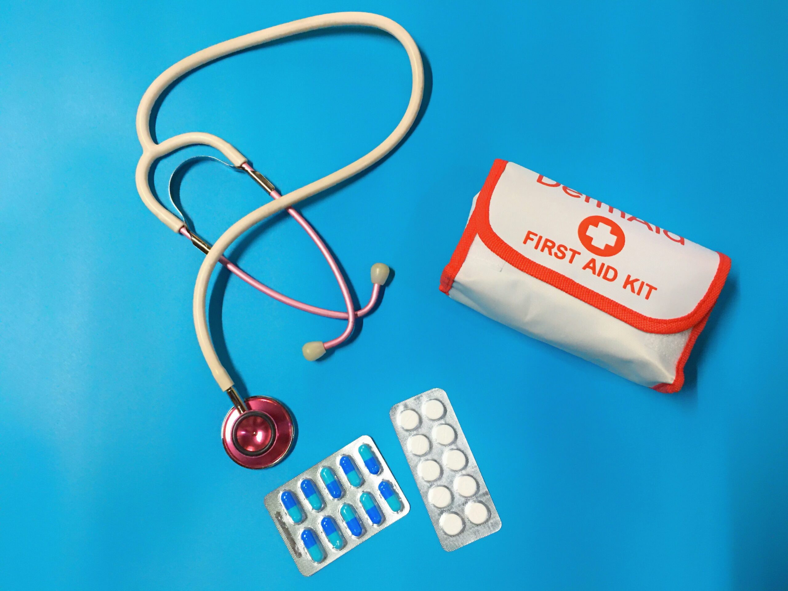 A first aid kit, stethoscope, and medication are arranged on a blue background, emphasizing preparedness and essential steps for handling injuries.