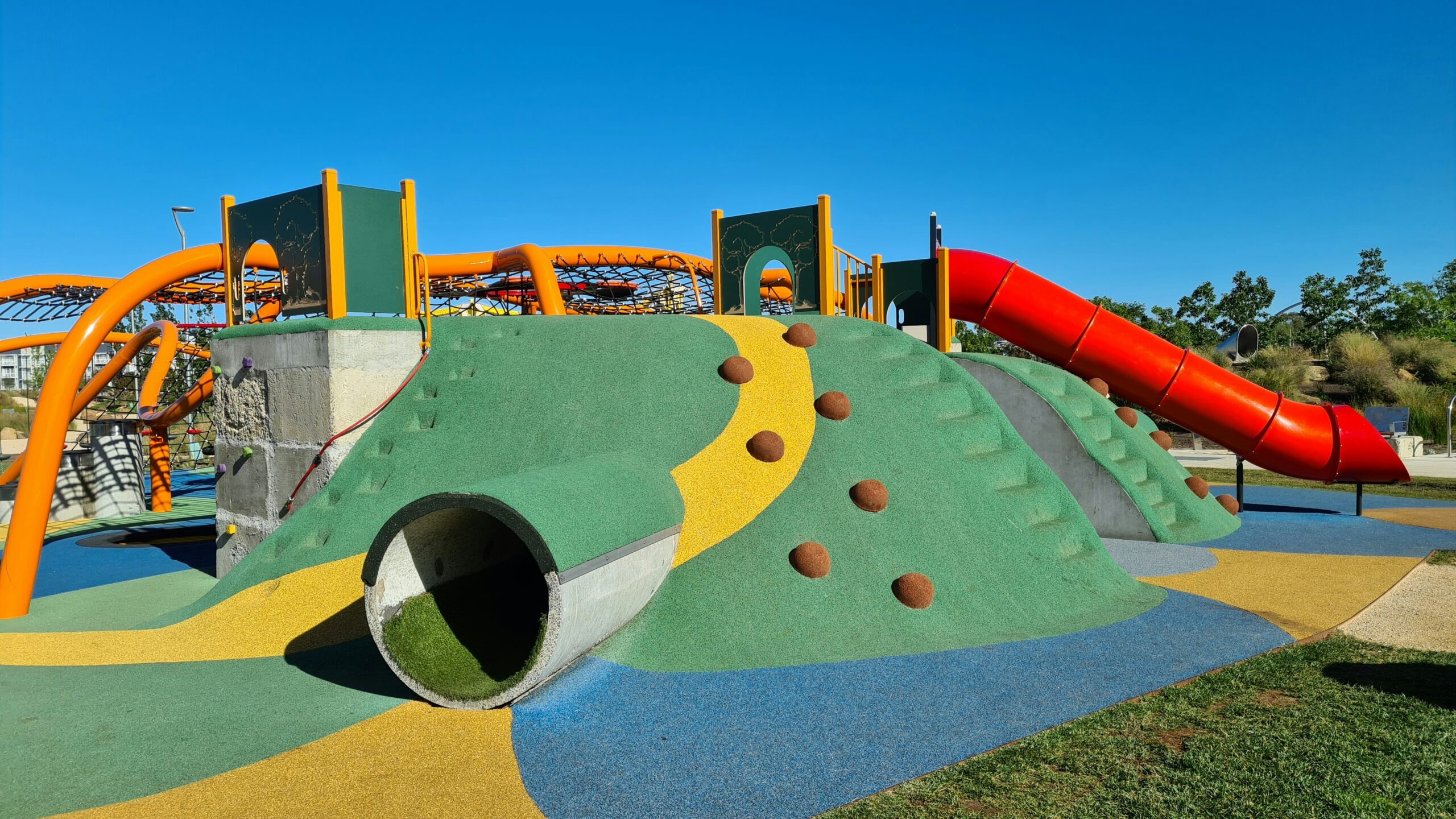 Colorful playground with climbing features and a red tube slide under a clear blue sky, highlighting an ideal setting for safe and fun Nerf battles.