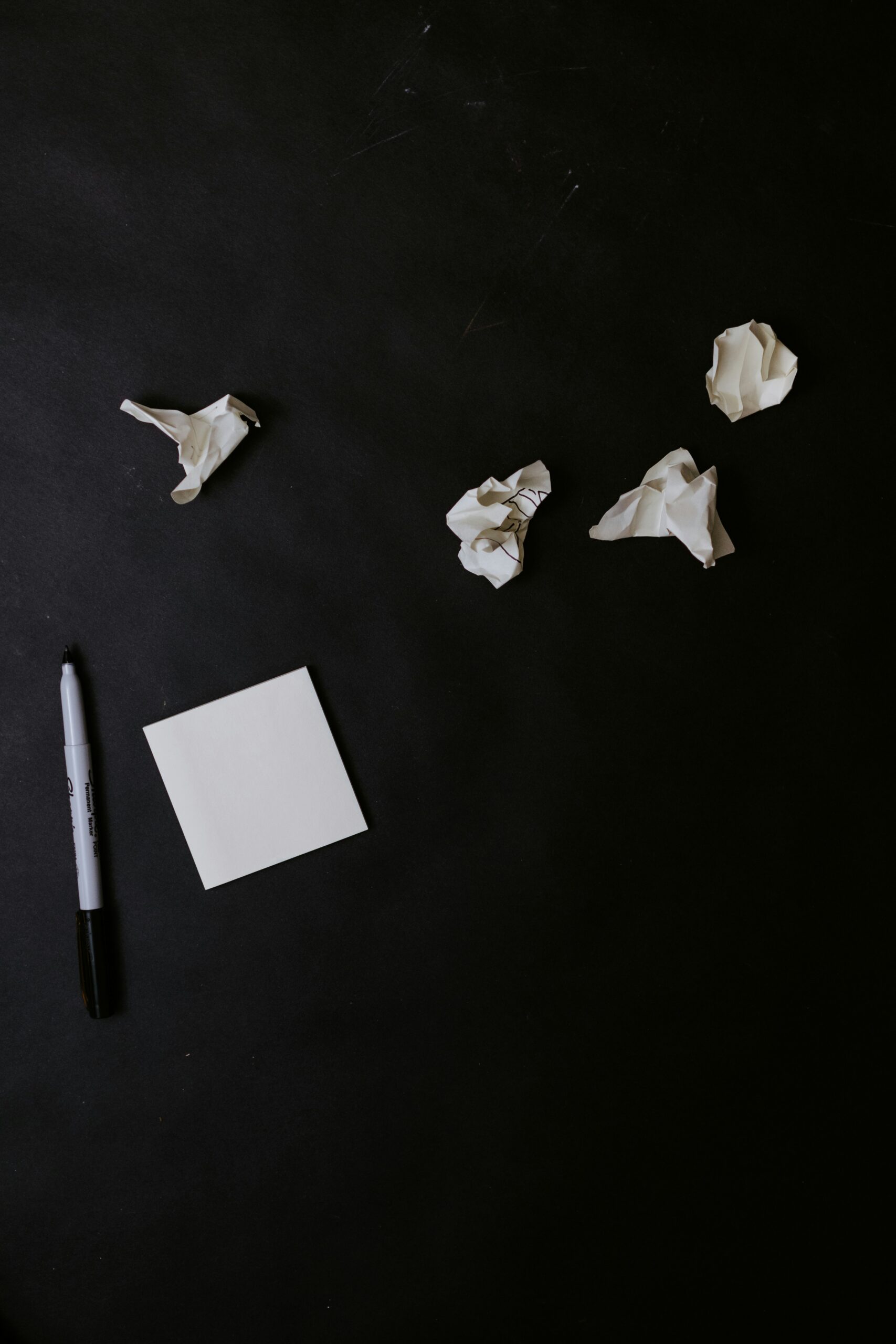 A blank notepad with a marker and crumpled paper on a dark surface, symbolizing brainstorming.