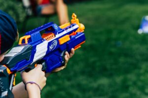 A person aiming a blue and orange Nerf blaster in an outdoor setting, demonstrating engaging rules and game mechanics for an exciting Nerf battle.