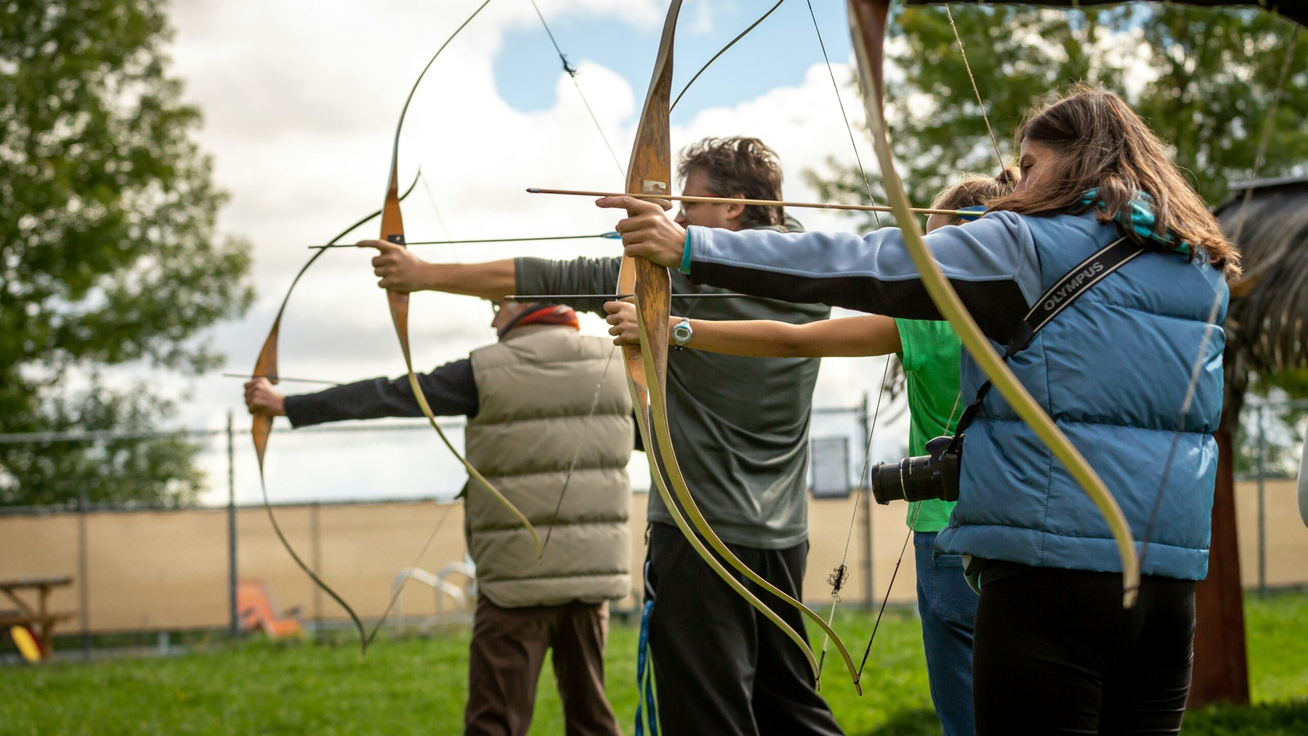 A group of players draws their bows in unison on a grassy field, illustrating the importance of organizing a clear and safe archery tag playing area. - Brainy Actz Escape Rooms A group of players draws their bows in unison on a grassy field, illustrating the importance of organizing a clear and safe archery tag playing area.
