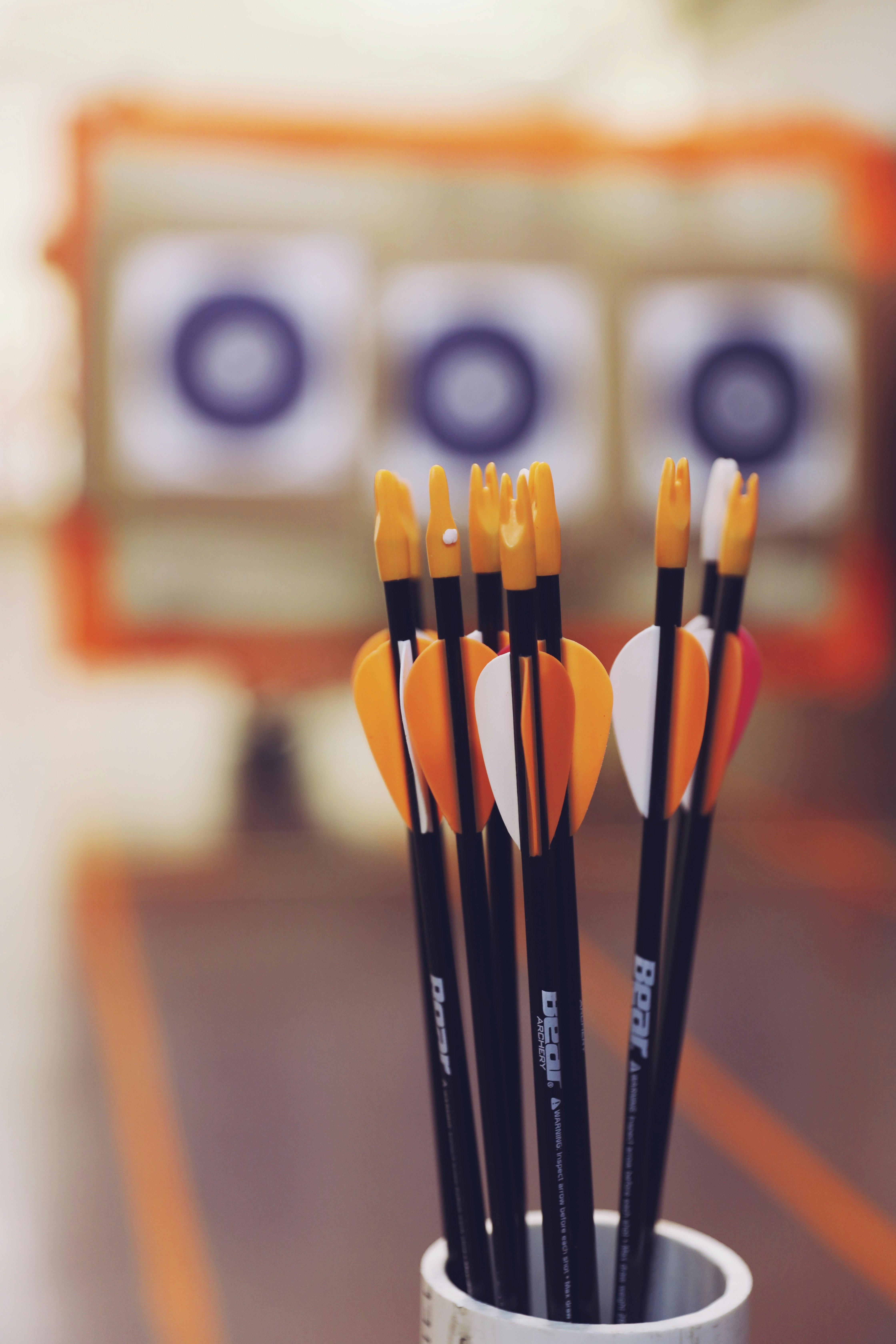 A container of arrows with targets in the background, emphasizing the need for clear conduct rules to ensure fair and safe archery tag play. - Brainy Actz Escape Rooms A close-up of target arrows with orange and white fletching in a holder, highlighting the need for proper storage and regular inspection to maintain arrow integrity.