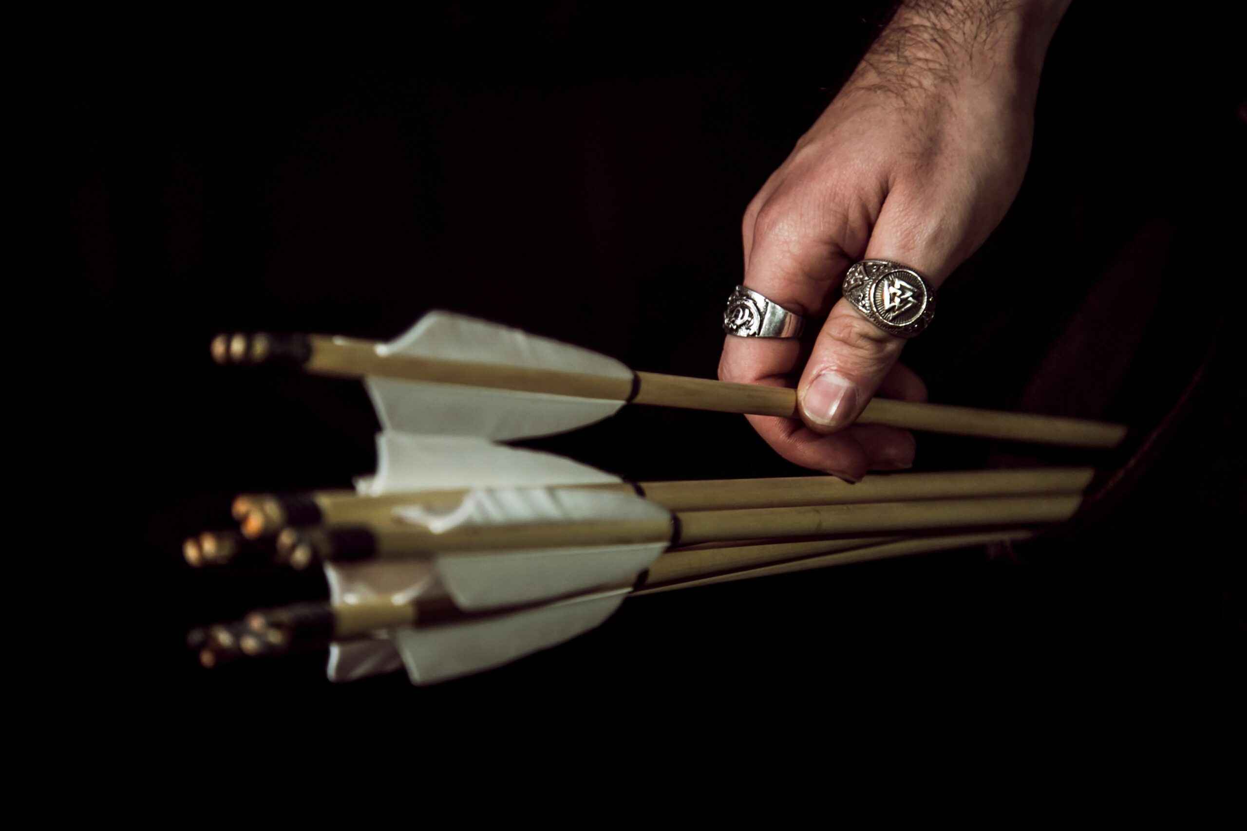 A close-up of a hand holding several wooden arrows with white fletching, emphasizing the importance of inspecting equipment for safety before use. - Brainy Actz Escape Rooms A close-up of a hand holding several wooden arrows with white fletching, emphasizing the importance of inspecting equipment for safety before use.