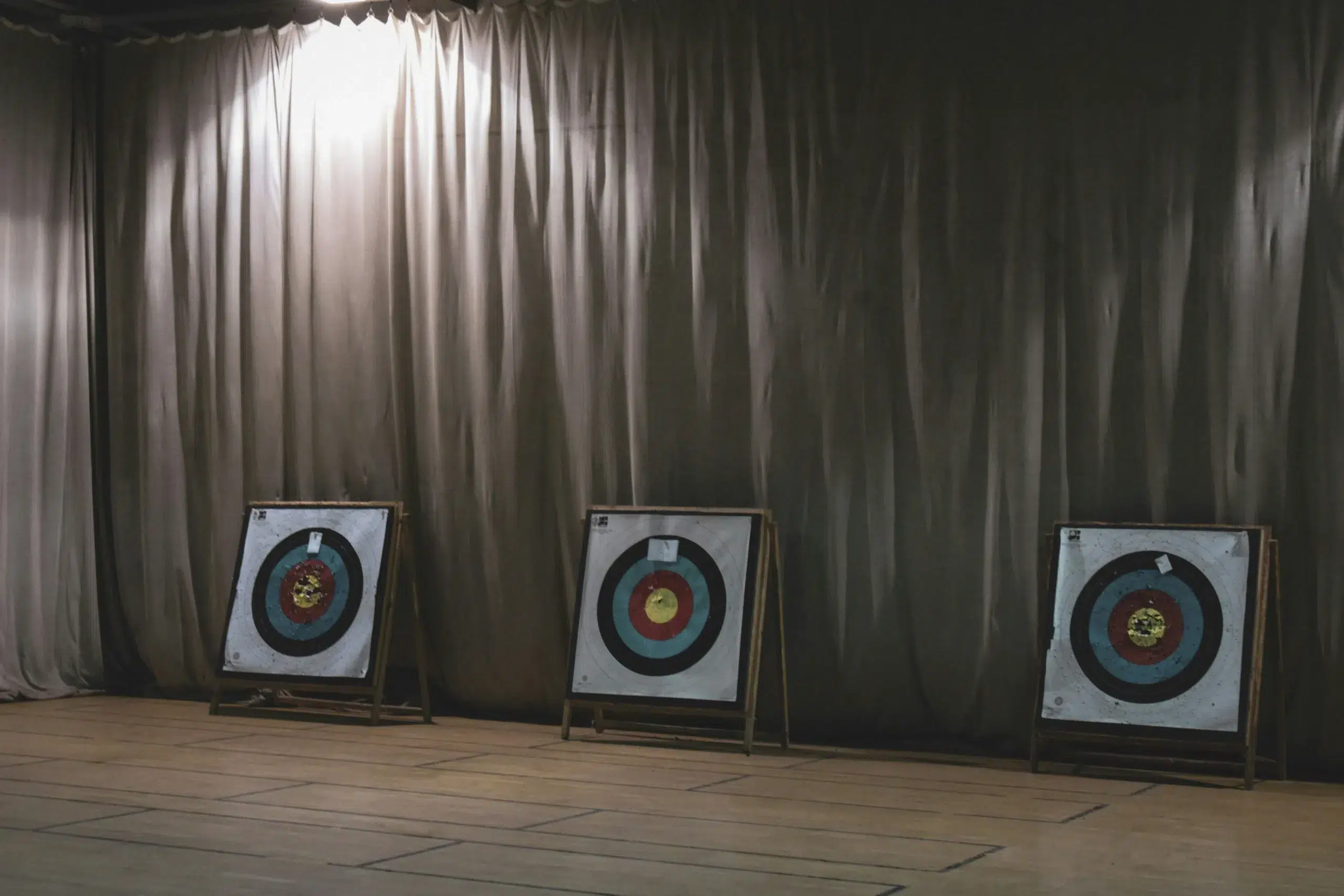Three freestanding archery targets with concentric ring designs are set up indoors, illustrating essential elements of versatile Archery Tag target systems. - Brainy Actz Escape Rooms Three freestanding archery targets with concentric ring designs are set up indoors, illustrating essential elements of versatile Archery Tag target systems.