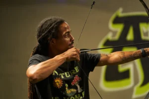 A focused player draws a bow with precise aim, highlighting the concentration, form, and skill essential for success in Archery Tag target competitions. - Brainy Actz Escape Rooms A focused player draws a bow with precise aim, highlighting the concentration, form, and skill essential for success in Archery Tag target competitions.