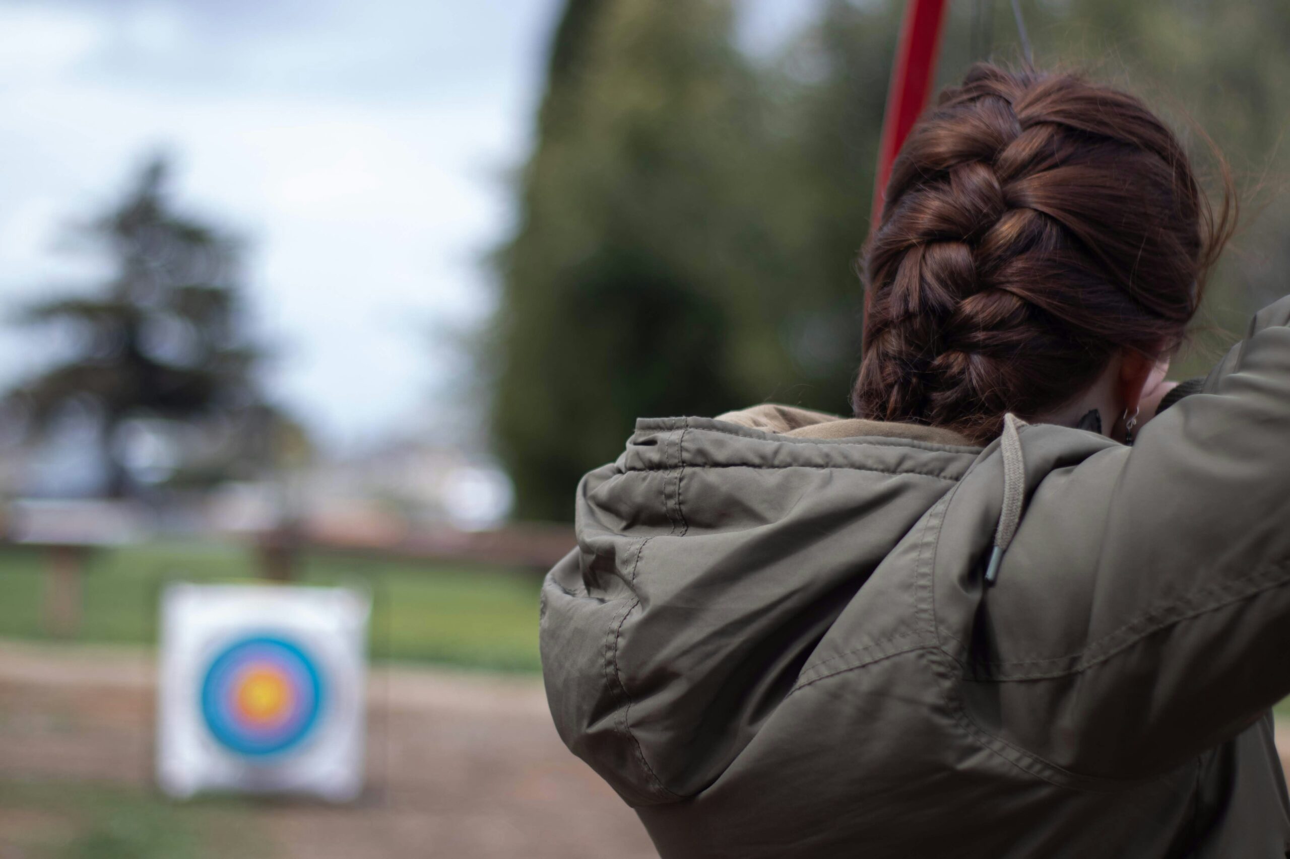 A person aims at a distant archery target outdoors, illustrating the importance of precise alignment and methodical setup when assembling custom Archery Tag targets.