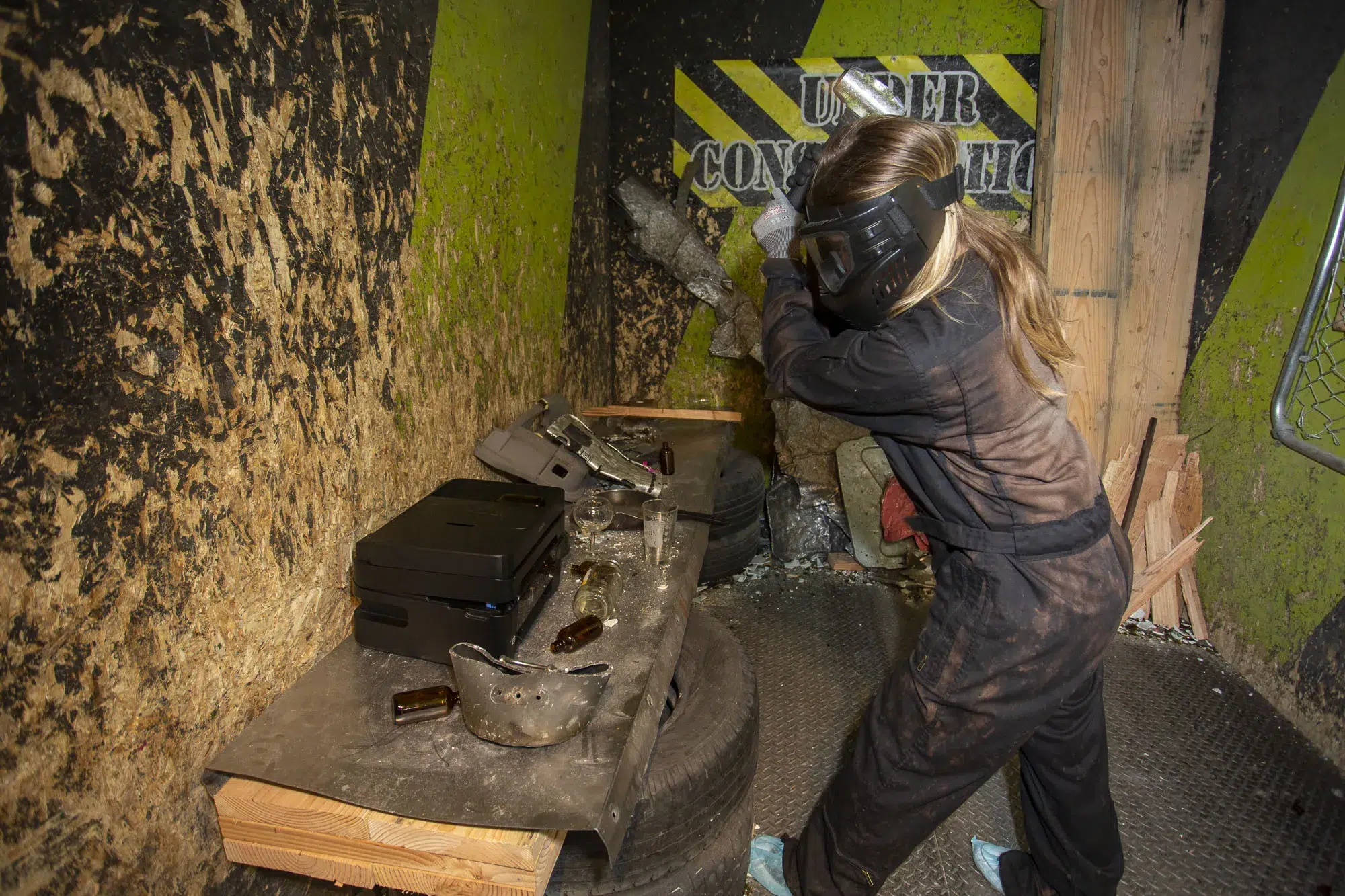 A person wearing full protective gear swings a bat inside a rage room—demonstrating how strict safety protocols like helmets, gloves, and coveralls protect participants during high-impact activities.