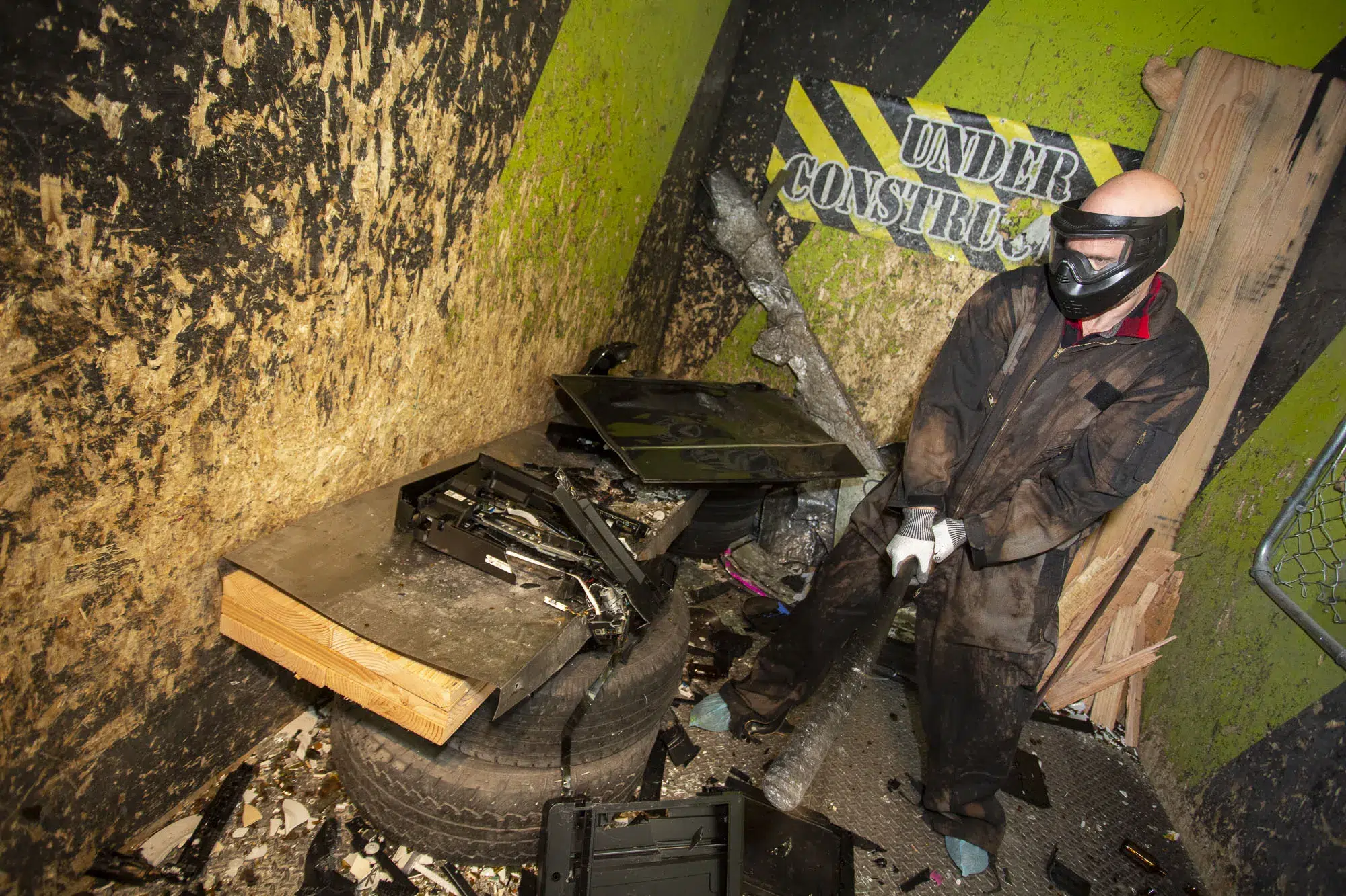 A person in protective gear smashing electronics in a rage room, promoting teamwork through shared release and collaboration.