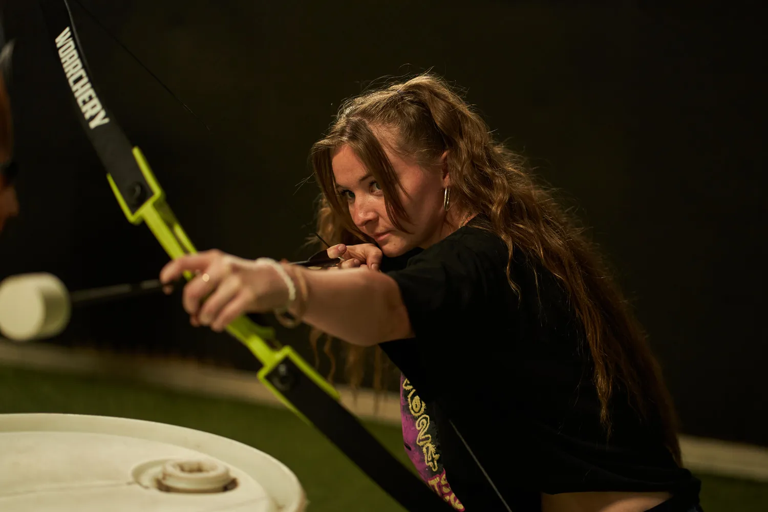 Focused Arrow Tag player draws her foam-tipped arrow, demonstrating how individual positioning supports foundational principles in strategic team formations. - Brainy Actz Escape Rooms Focused Arrow Tag player draws her foam-tipped arrow, demonstrating how individual positioning supports foundational principles in strategic team formations.