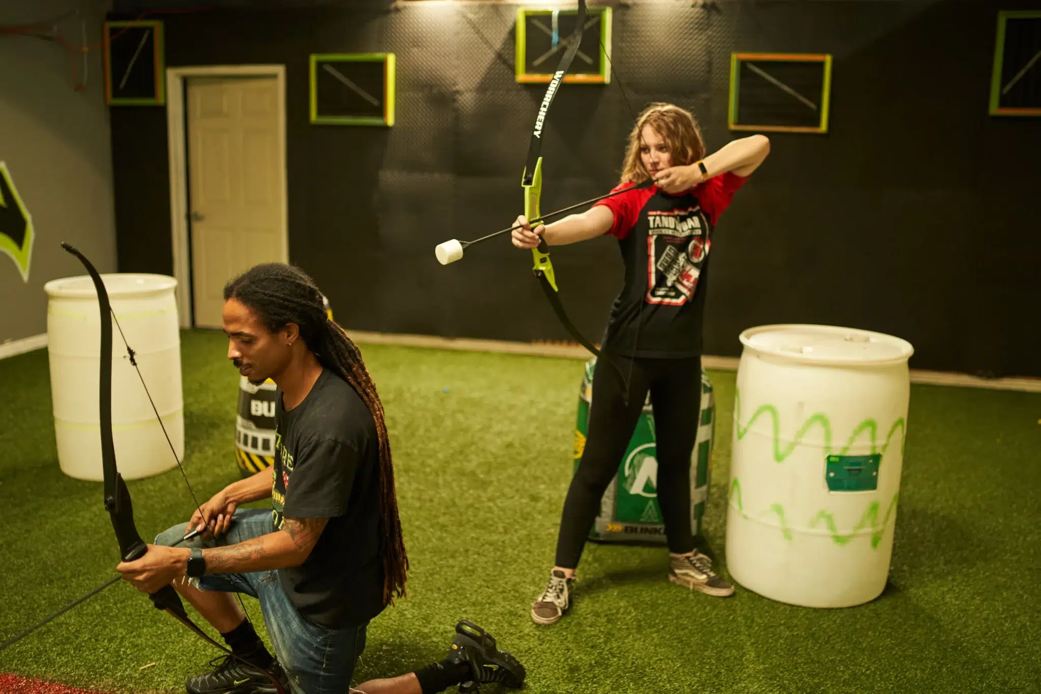 Two arrow tag players demonstrate strategic teamwork as one provides covering fire while the other prepares a shot, highlighting effective role assignment in collaborative play.